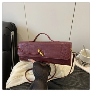 Detail of burgundy baguette bag with croc-embossed texture and golden twist-lock buckle