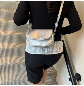 Silver metallic crossbody bag with semi-circle flap design on a model at waist height