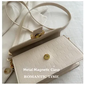 Dettaglio della chiusura magnetica dorata su borsa beige con motivo a coccodrillo