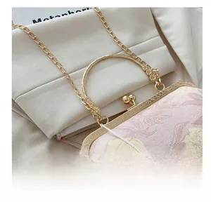 Close-up of golden hardware, floral fabric, and white lotus tassel on a crossbody bag