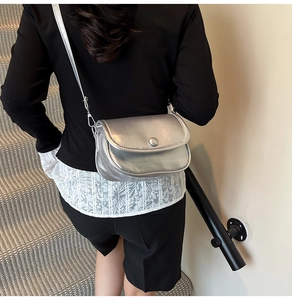 Silver metallic saddle bag with curved flap and magnetic closure on female model