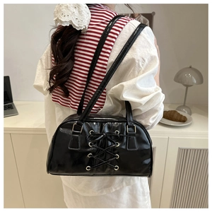 Detail of black patent leather bag with lace-up bow design worn as an underarm bag