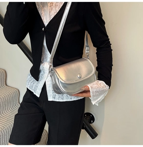 Close-up of a glossy silver metallic crossbody bag worn by a model in a minimal setting