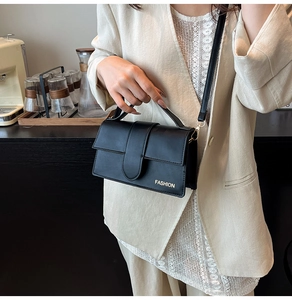 Detail of black rectangular crossbody bag with FASHION text in a modern cafe setting