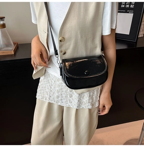 Close-up of black glossy half-moon crossbody bag with elegant flap and leather strap