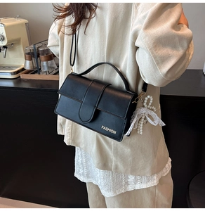 Detail of a black PU leather bag with a gold Fashion logo and a pearl lace charm