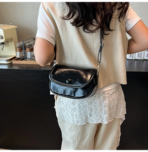 Detail of a black glossy crossbody bag with adjustable strap in a cafe setting