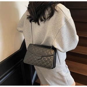 Détail d'un sac bandoulière noir matelassé avec chaîne en métal porté par un modèle