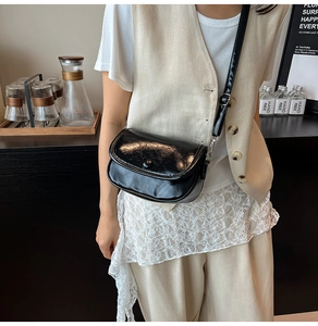 Close-up of a glossy black saddle bag with adjustable leather strap worn by a model