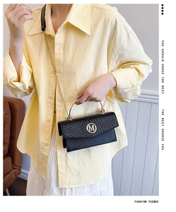 Detail of black woven flap bag with gold M-logo and metallic handle on model