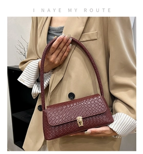 Close-up of woven leather texture and golden metal buckle on burgundy shoulder bag