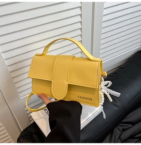 Detail of yellow leather crossbody bag featuring pearl charm and bow accessory