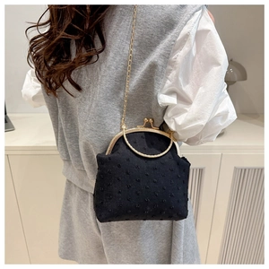 Detalle del bolso negro de lunares con cadena y cierre dorado mostrado por una modelo