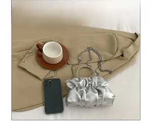 Detail of silver pleated handbag with rhinestone handle and metal chain on a table