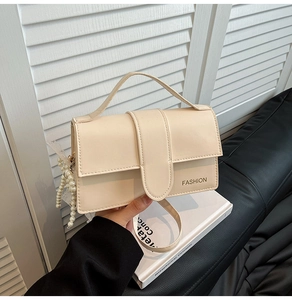 Close-up of cream crossbody bag with FASHION logo and pearl lace pendant detail