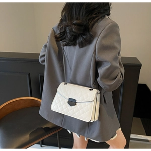 Détail d'un sac à chaîne en cuir matelassé blanc porté par un mannequin en veste