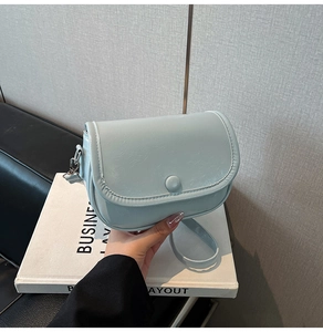 Close-up of light blue saddle bag featuring a smooth flap and round buckle detail