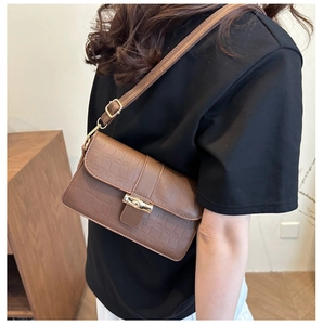 Detail of a brown crocodile embossed underarm bag featuring a golden twist-lock closure