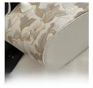 Macro view of grey and gold floral embroidery and precision stitching on white leather bag