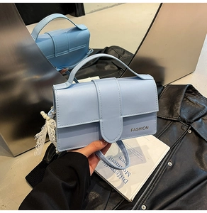 Detail of light blue crossbody bag with lace pearl charm and fashion logo print