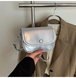 Close-up of metallic silver mini saddle bag with textured pleats and round buckle