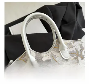 Detail shot of elegant floral embroidery and smooth white handle on the fashion handbag