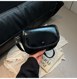 Close-up of elegant black patent leather shoulder bag with glossy finish and snap closure