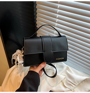 Close-up of black PU handbag featuring gold FASHION lettering and pearl lace charms