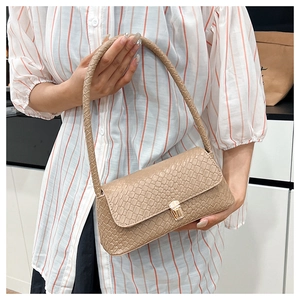 Close-up of beige woven texture and gold clasp on minimalist flap baguette bag