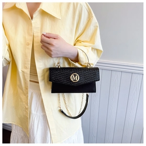 Detail of woven texture flap with gold M logo and chain strap on black crossbody bag