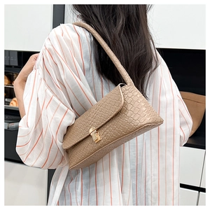 Close-up of woven khaki baguette bag featuring a metallic lock buckle on a shoulder strap