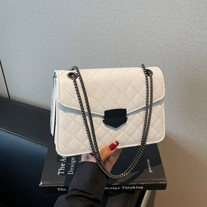 Sac bandoulière blanc matelassé avec chaîne et boucle noire sur un livre de design