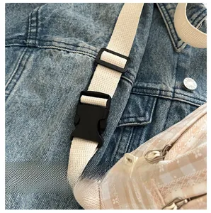 Detail of black plastic buckle and beige strap on a pink plaid crossbody bag