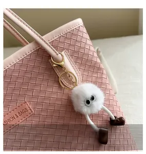 Close-up of a cute white plush bag charm with big eyes on a pink woven tote bag