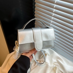 Silver mirror finish crossbody bag with pearl lace pendant and top handle on white background