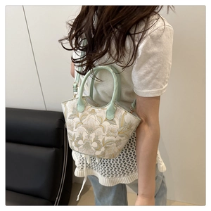 Detail of floral embroidery on a small bucket bag with a light green cylindrical handle