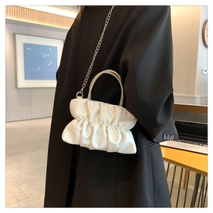 Close-up of white pleated handbag featuring rhinestone-studded handle and silver chain