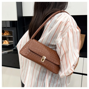 Detail of brown woven texture handbag with golden swivel lock worn on shoulder
