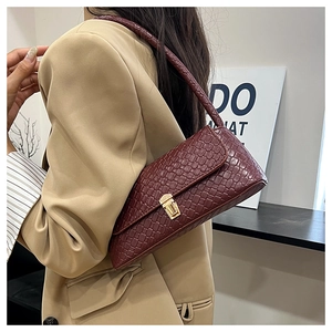 Close-up of burgundy baguette bag with crocodile texture and gold buckle on shoulder