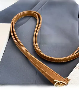 Detail of brown leather strap with contrast white stitching and gold metal buckle hardware