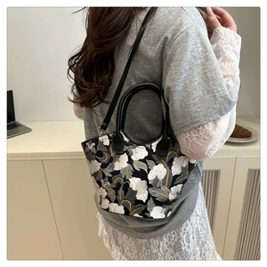 Detail showing vintage floral embroidery on a crossbody bag with black handle