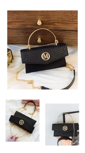Detail view of black handbag showing gold M logo and metallic handle on woven texture
