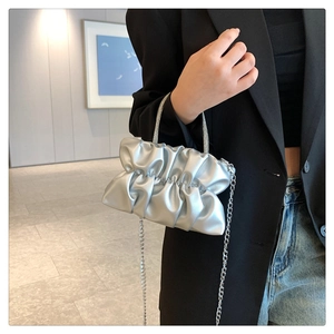 Silver pleated cloud bag featuring rhinestone handle and metal chain on model