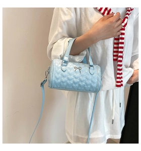 Detalle de bolso cilíndrico azul claro con acolchado de corazones y colgante de lazo
