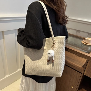 Detail of cream woven tote bag with a cute plush doll charm and metallic brand plaque