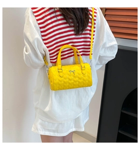 Detailed view of yellow cylinder bag featuring heart quilting and a silver bow detail