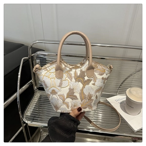 Close-up of floral embroidery detail and cylindrical leather handle on beige bucket bag