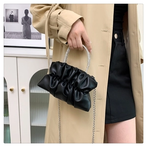 Close-up of black pleated bag featuring rhinestone handle and silver metal chain strap