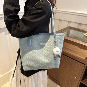 Close-up of light blue woven tote bag with a white plush doll charm and textured detail