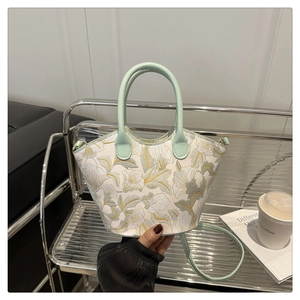 Detail of floral embroidery on a white fabric bucket bag with light green leather handle